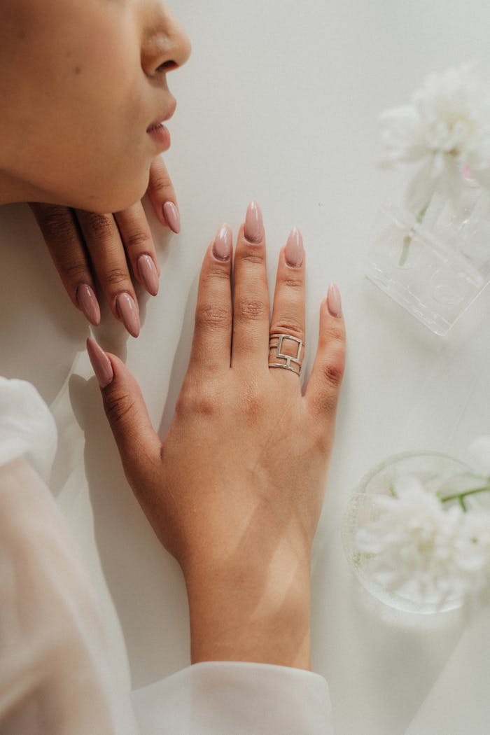 Close-up of a woman's manicured hand with jewelry on a white table.